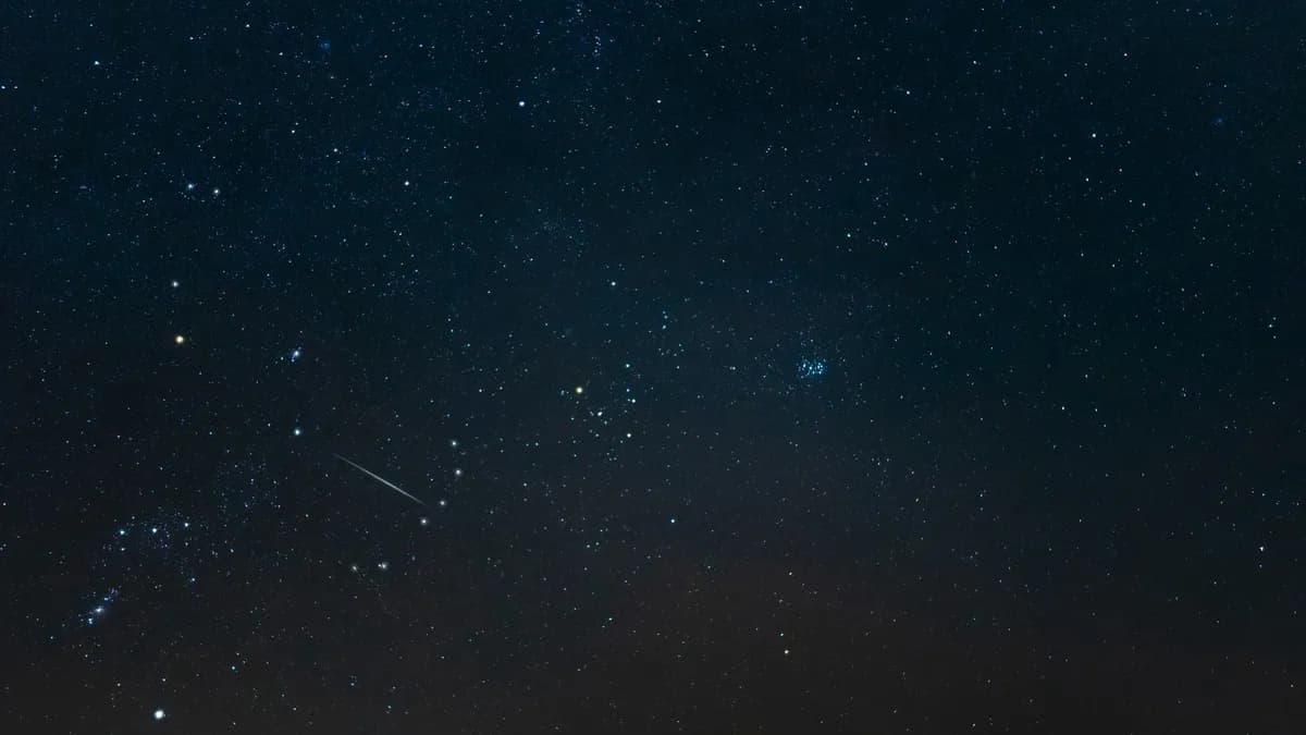 Céu noturno estrelado com as estrelas de Órion à esquerda e, no centro, um pequeno grupo em forma de V em torno de uma estrela alaranjada; à direita, um aglomerado compacto azulado.