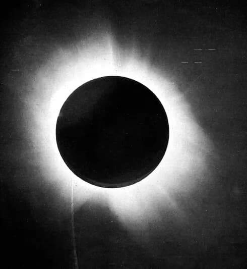 Fotografia em preto e branco do Sol totalmente eclipsado: um disco negro cercado pela coroa solar esbranquiçada, contra o céu escuro.