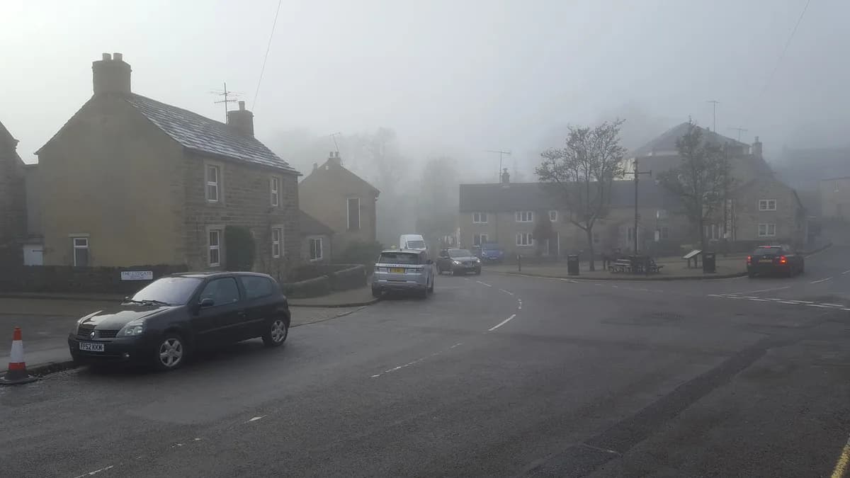 Vista do vilarejo de Eyam, em Derbyshire, na Inglaterra, com casas de pedra e colinas verdes do Peak District ao fundo.