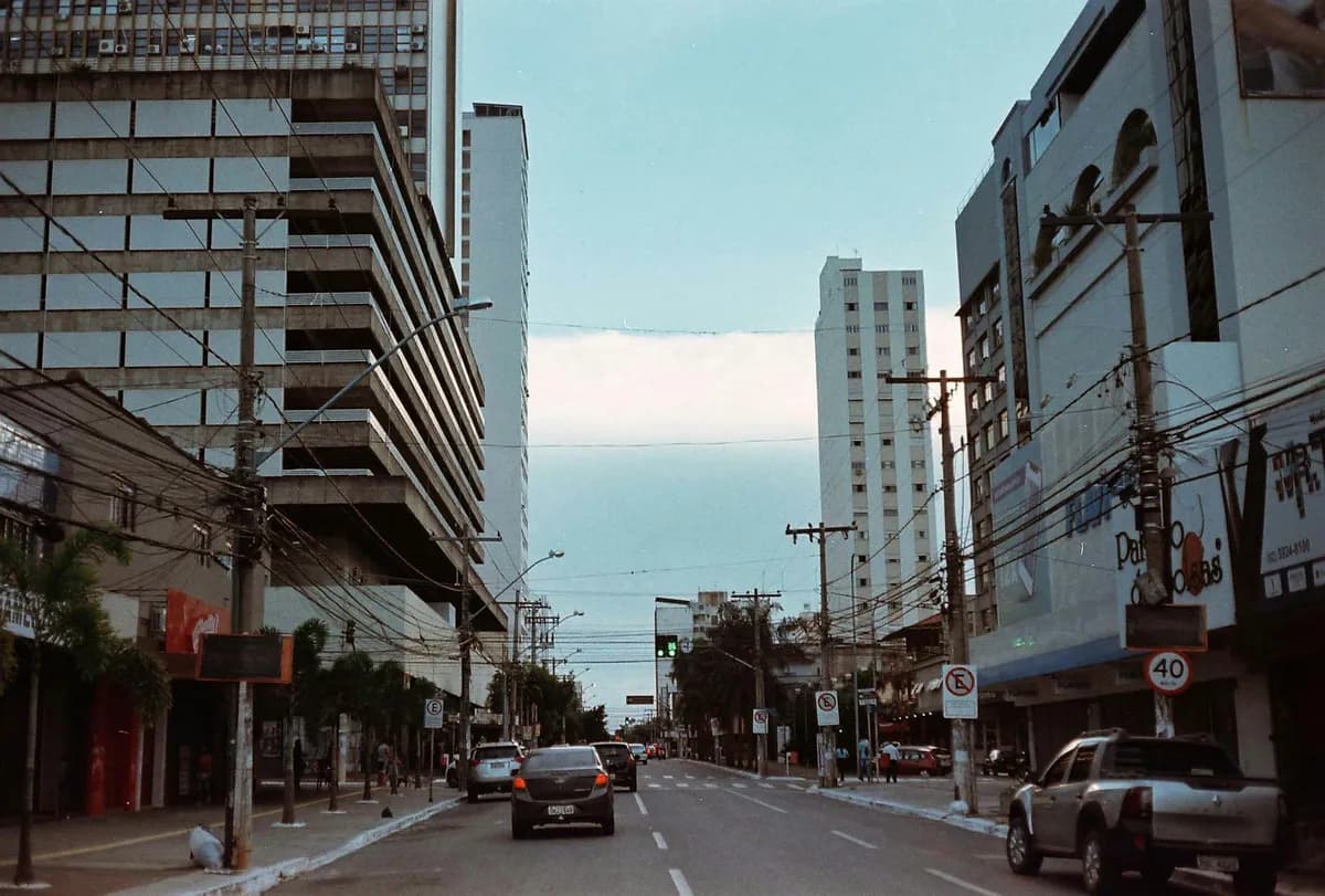 Avenida de Goiânia com carros, postes cheios de fios e prédios de escritórios e apartamentos dos dois lados, sob céu nublado.