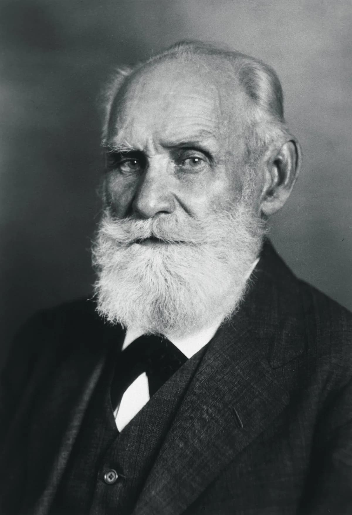 Retrato fotográfico de Ivan Pavlov, fisiologista russo, de barba branca e jaleco, em seu laboratório.