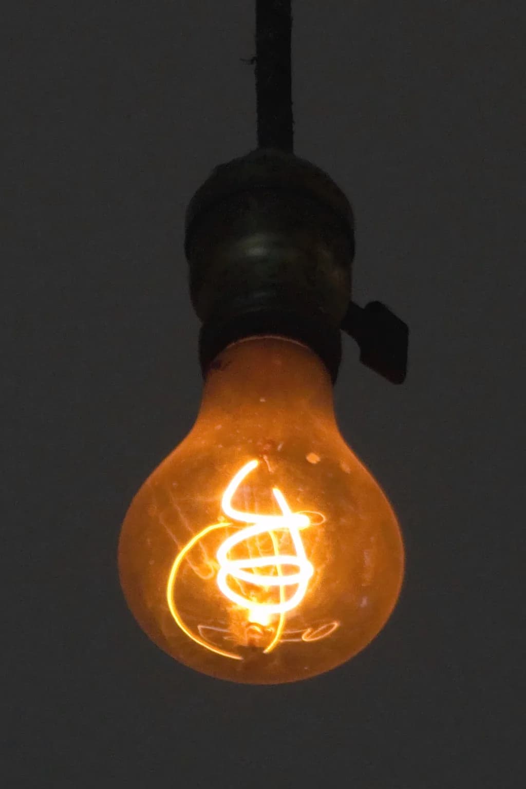 A lâmpada centenária de Livermore, na Califórnia, pendurada no teto do quartel de bombeiros, com filamento de carbono aceso em brilho alaranjado fraco.