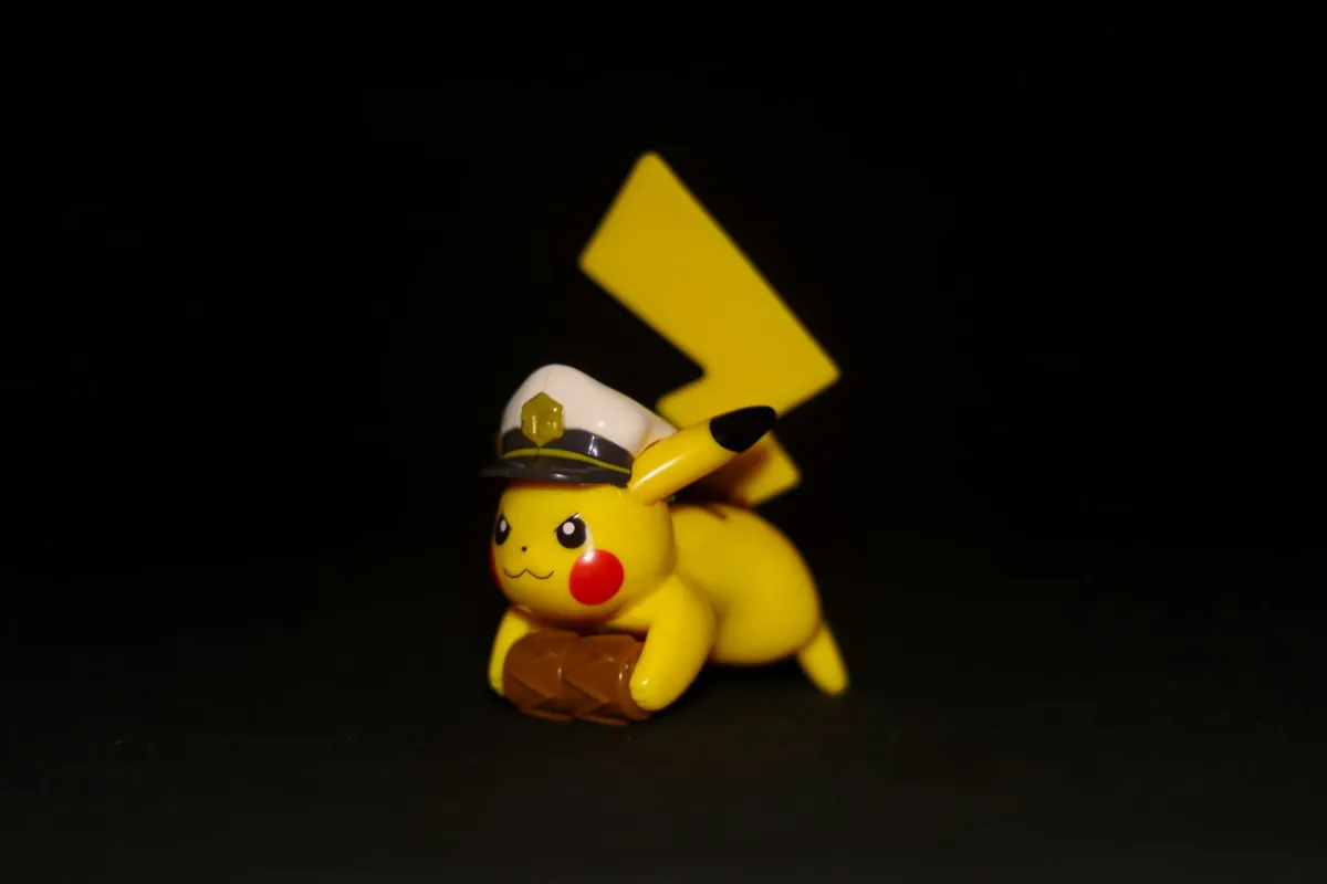 Boneco do Pikachu deitado, com quepe branco de marinheiro, sobre fundo preto; a cauda em forma de raio aparece inteira atrás dele.