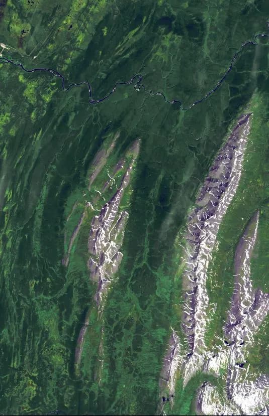 Imagem de satélite em cores falsas mostrando cristas de montanha alongadas e esbranquiçadas no sentido norte-sul, cercadas por vales verdes e um rio sinuoso no alto.