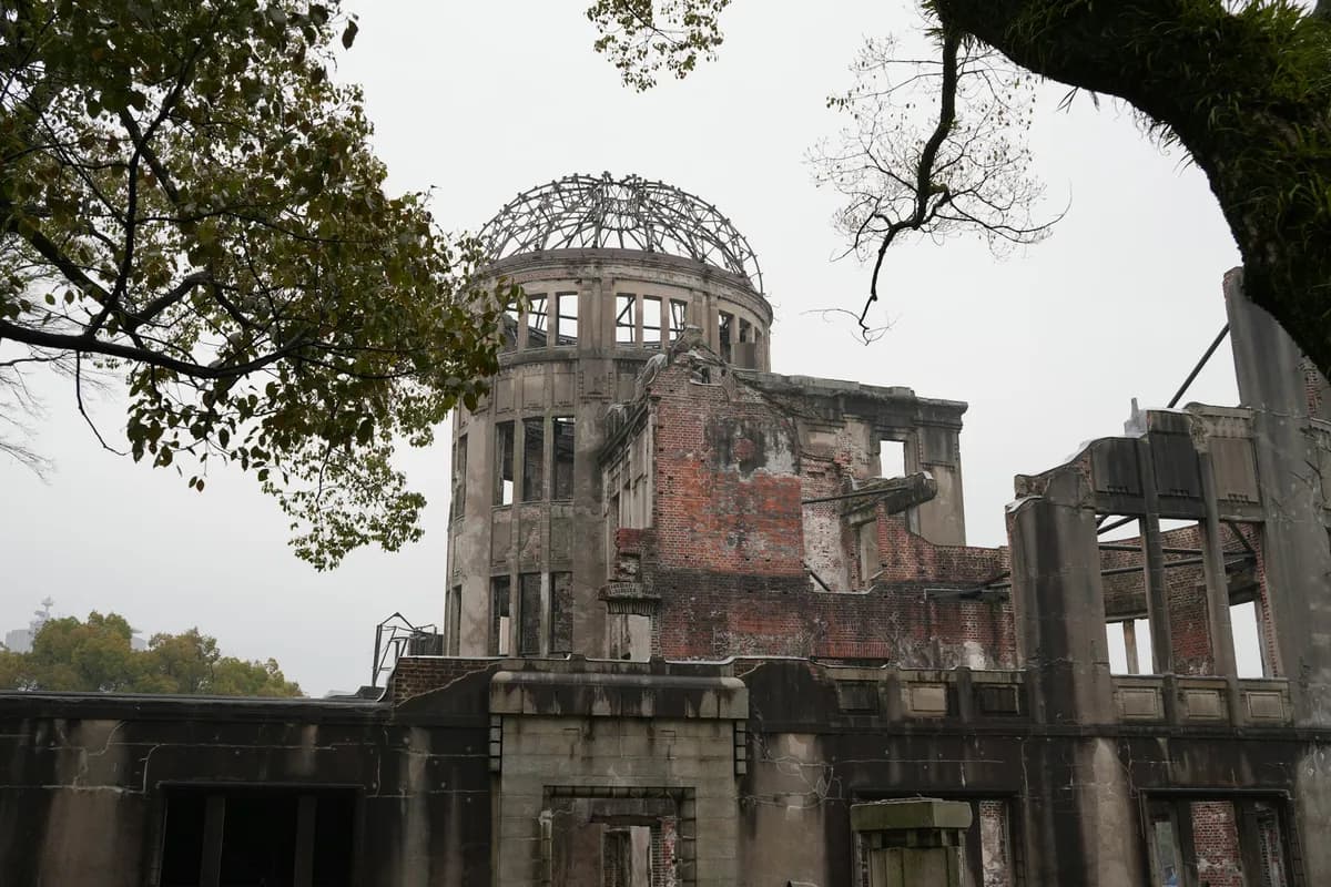 Ruína de um prédio de tijolos e concreto com a estrutura metálica de uma cúpula exposta no alto, entre galhos de árvores, sob céu nublado.